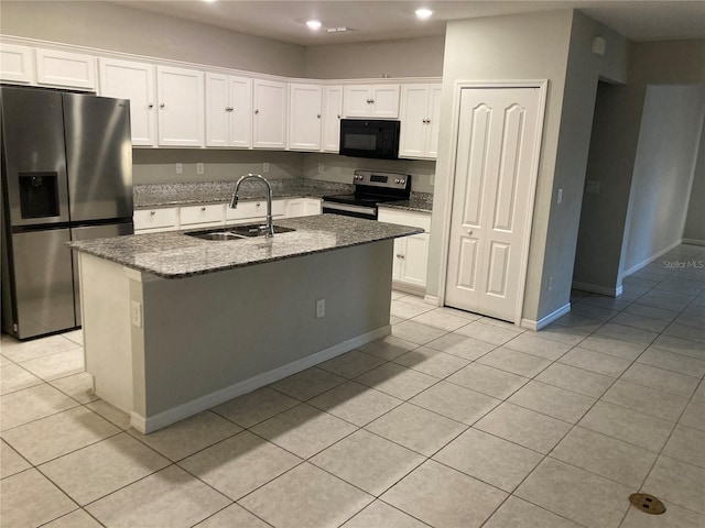 kitchen featuring a center island with sink, appliances with stainless steel finishes, white cabinetry, a sink, and dark stone counters