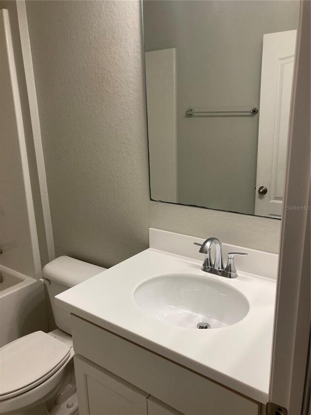 full bath featuring toilet, vanity, and a textured wall