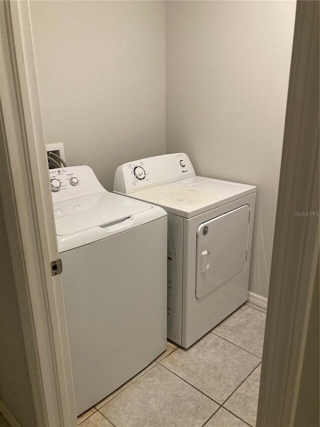 clothes washing area with laundry area, light tile patterned floors, baseboards, and washer and clothes dryer