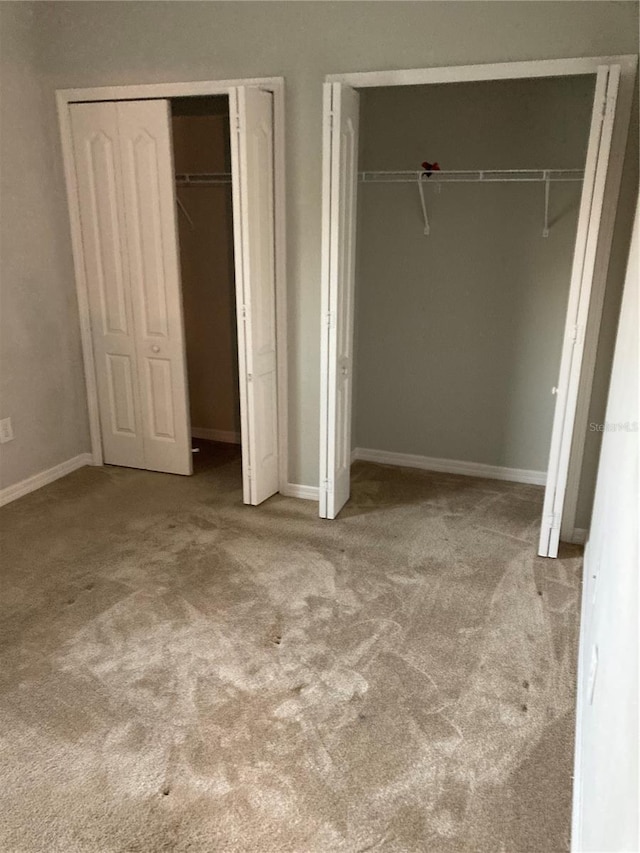 unfurnished bedroom with light colored carpet, baseboards, and two closets