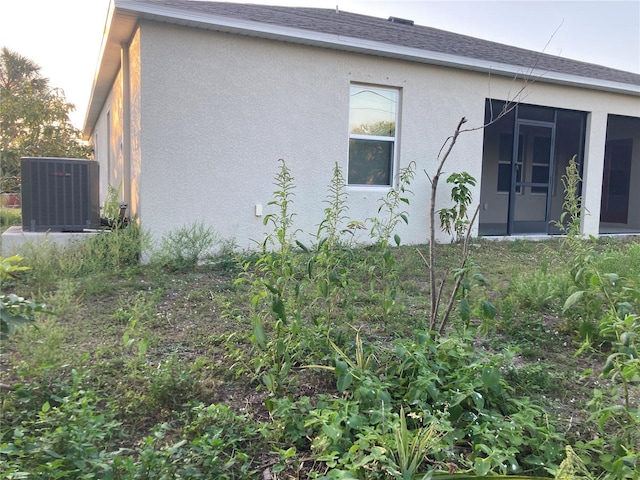 exterior space featuring central AC, roof with shingles, and stucco siding