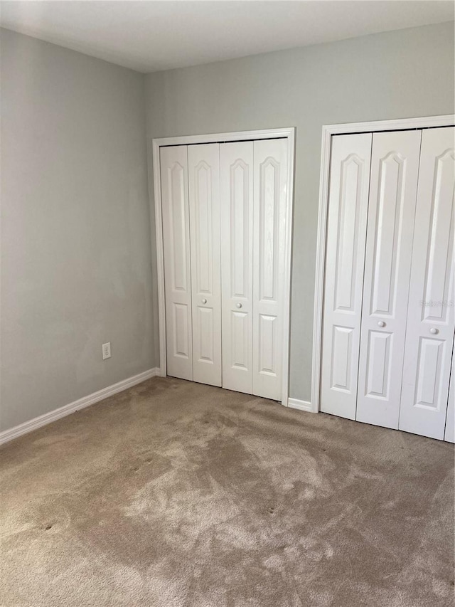 unfurnished bedroom featuring carpet floors, baseboards, and two closets