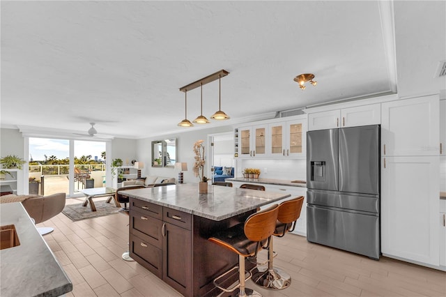 kitchen featuring decorative light fixtures, white cabinetry, a center island, stainless steel refrigerator with ice dispenser, and light stone countertops