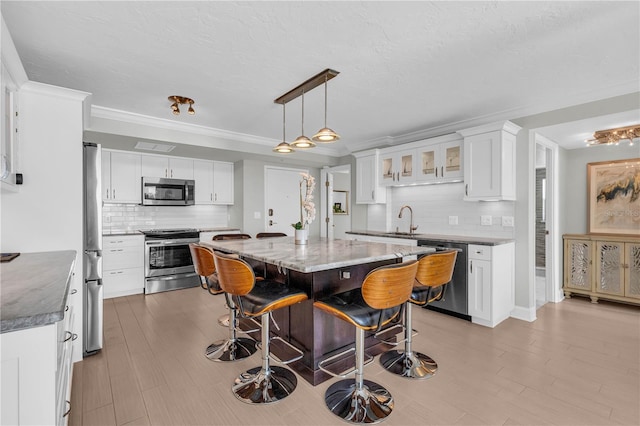 kitchen with light stone counters, a kitchen island, pendant lighting, stainless steel appliances, and white cabinets