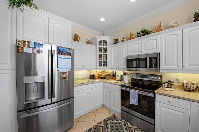 kitchen with light tile patterned flooring, ornamental molding, appliances with stainless steel finishes, and white cabinets