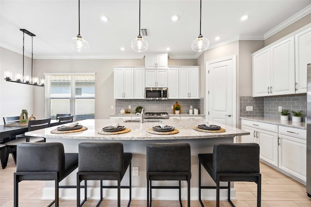 kitchen featuring a kitchen island with sink, sink, white cabinets, and decorative light fixtures