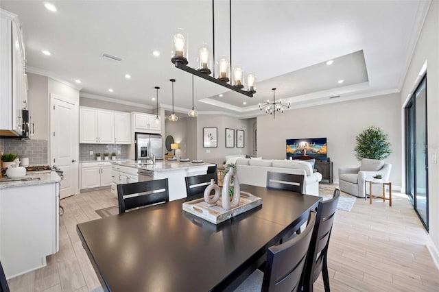 dining area with a raised ceiling, ornamental molding, and light hardwood / wood-style flooring