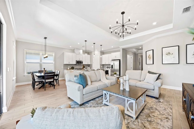 living room featuring crown molding, a tray ceiling, light hardwood / wood-style flooring, and a chandelier