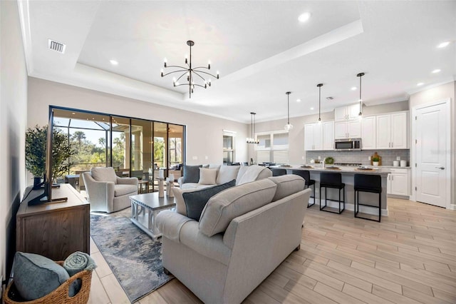 living room with a chandelier, ornamental molding, a raised ceiling, and light hardwood / wood-style flooring