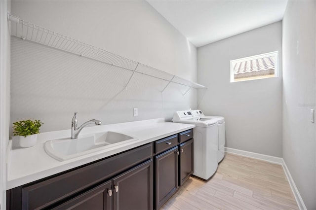 clothes washing area featuring light hardwood / wood-style floors, sink, cabinets, and washer and dryer