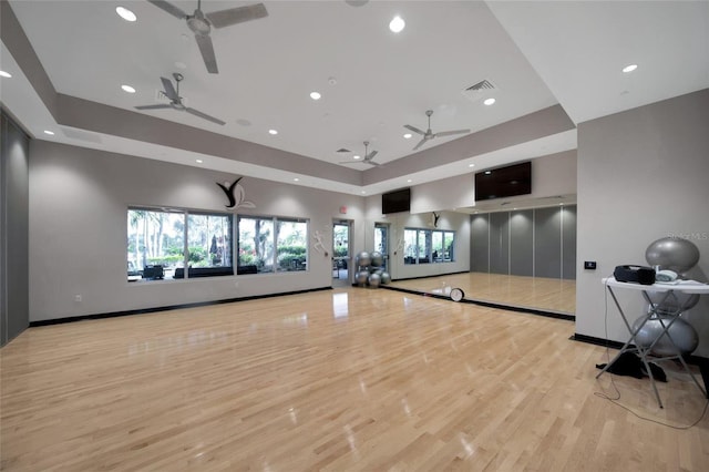 exercise room featuring ceiling fan, light hardwood / wood-style floors, and a tray ceiling