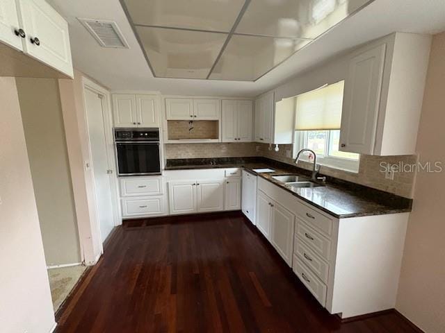 kitchen with dark countertops, visible vents, black oven, dark wood-style floors, and a sink