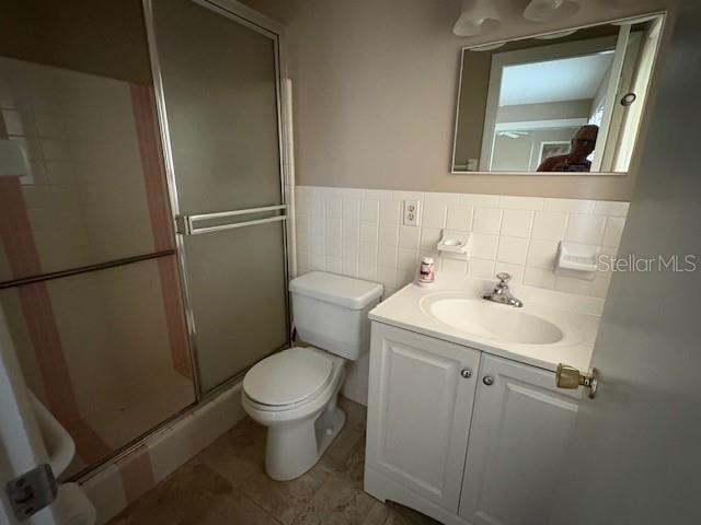 bathroom with vanity, a shower stall, wainscoting, tile walls, and toilet