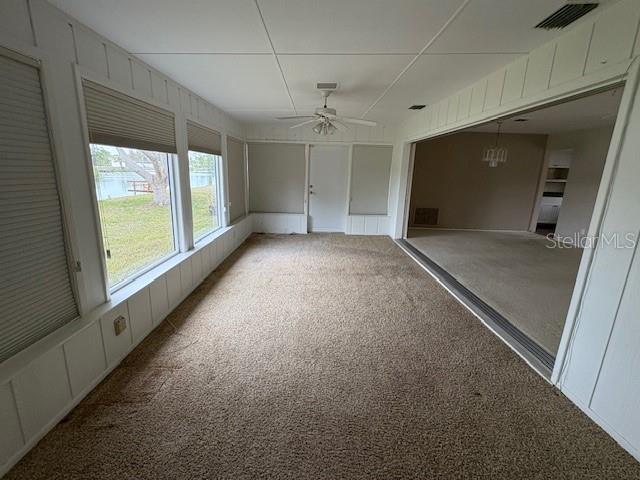 unfurnished room featuring a decorative wall, visible vents, carpet floors, and ceiling fan