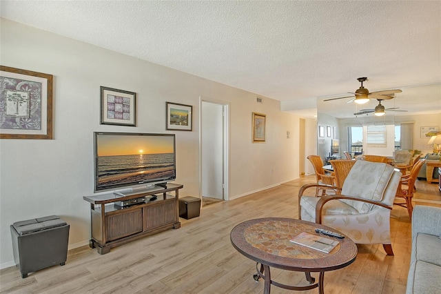 living room featuring ceiling fan, light hardwood / wood-style flooring, and a textured ceiling