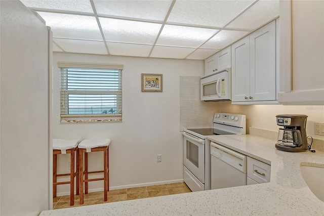 kitchen featuring a drop ceiling, white cabinets, white appliances, and light stone counters