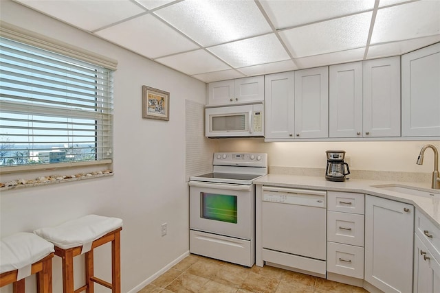 kitchen with white cabinets, white appliances, sink, and a drop ceiling