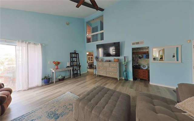 living room with beamed ceiling, wood-type flooring, and a towering ceiling