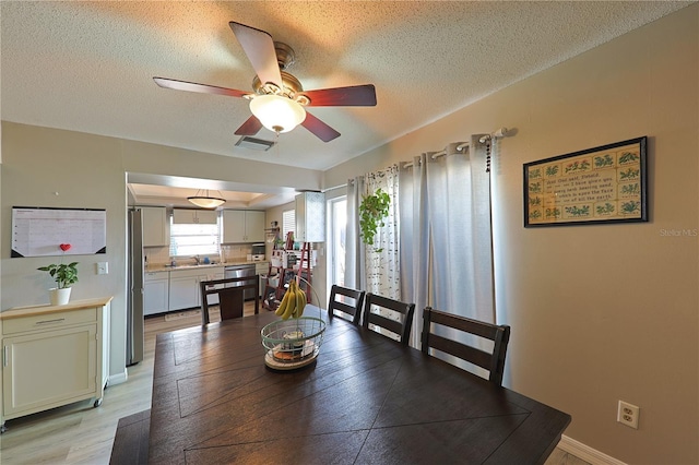 dining area with sink, light hardwood / wood-style floors, a textured ceiling, and ceiling fan