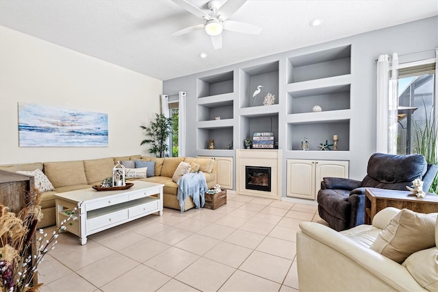 living area featuring light tile patterned floors, ceiling fan, a textured ceiling, built in features, and a glass covered fireplace