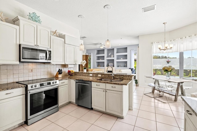 kitchen with pendant lighting, stainless steel appliances, visible vents, a sink, and dark stone counters