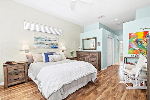 bedroom with ceiling fan, wood finished floors, visible vents, baseboards, and a closet