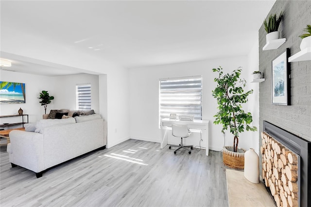 living room featuring a wealth of natural light, a brick fireplace, and light wood-type flooring