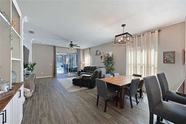 dining area with dark wood-type flooring, ceiling fan with notable chandelier, and a textured ceiling