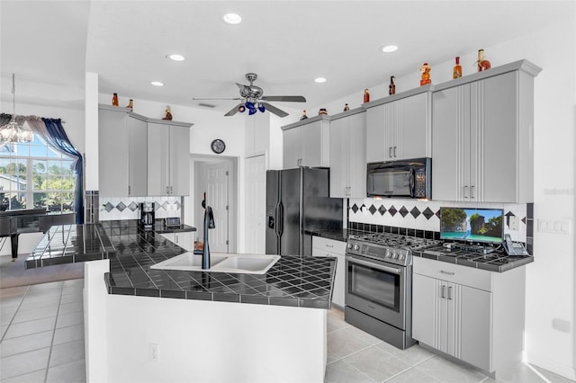 kitchen featuring sink, light tile patterned floors, black appliances, ceiling fan with notable chandelier, and kitchen peninsula