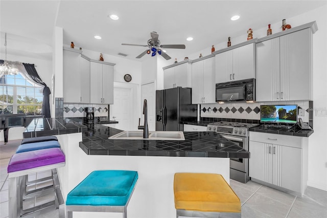 kitchen with black appliances, sink, a breakfast bar area, tile counters, and kitchen peninsula