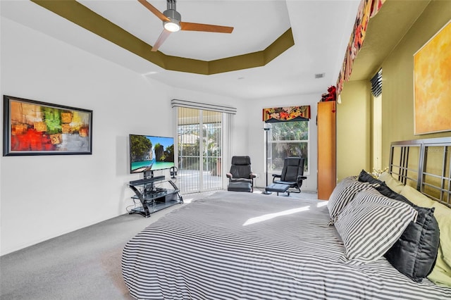 carpeted bedroom featuring access to exterior, ceiling fan, and a tray ceiling