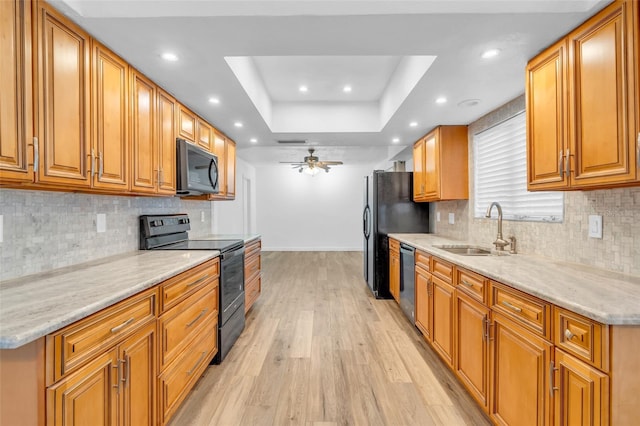 kitchen featuring sink, light hardwood / wood-style flooring, ceiling fan, black appliances, and a raised ceiling