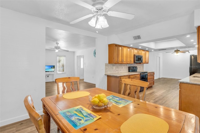 dining room with ceiling fan, a raised ceiling, and light hardwood / wood-style flooring