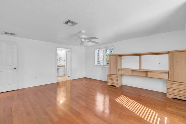 unfurnished living room featuring ceiling fan, built in desk, light hardwood / wood-style flooring, and a textured ceiling