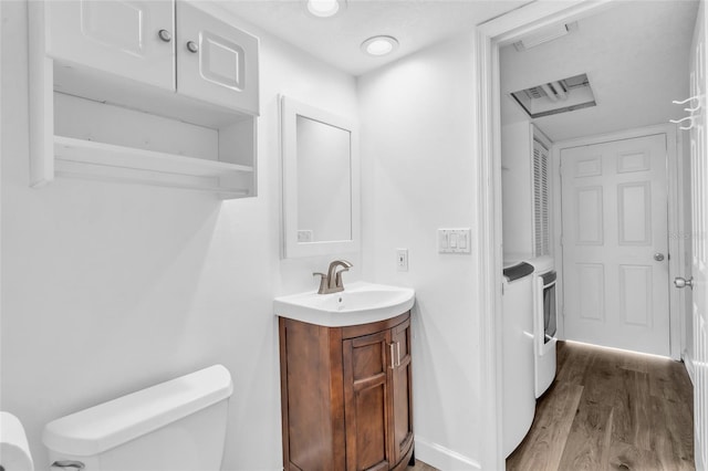 bathroom featuring hardwood / wood-style flooring, washing machine and clothes dryer, vanity, and toilet