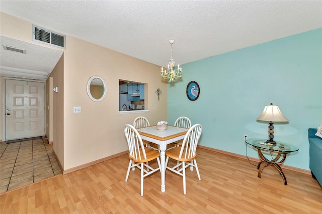 dining area featuring a textured ceiling, light hardwood / wood-style floors, and a chandelier