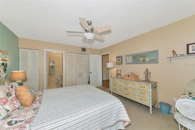 bedroom featuring connected bathroom, two closets, carpet floors, and a textured ceiling