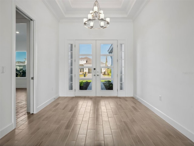 doorway to outside featuring crown molding, an inviting chandelier, light hardwood / wood-style floors, and a tray ceiling