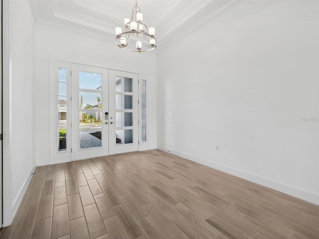 interior space with a tray ceiling, light hardwood / wood-style flooring, ornamental molding, and french doors