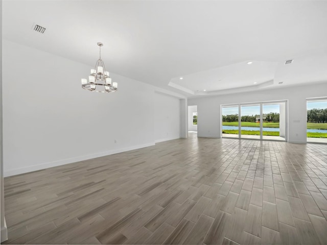 unfurnished living room with hardwood / wood-style flooring, a chandelier, and a tray ceiling