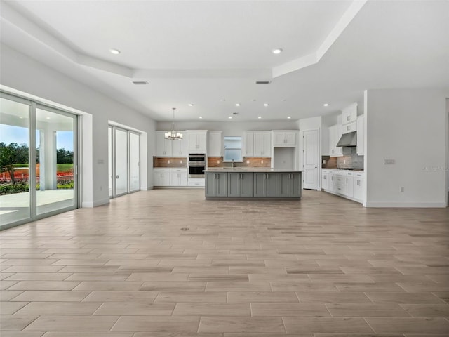 unfurnished living room with a raised ceiling, sink, a chandelier, and light hardwood / wood-style flooring