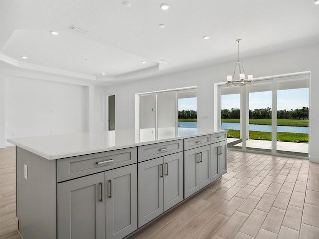 kitchen with gray cabinetry, a water view, decorative light fixtures, a raised ceiling, and a kitchen island