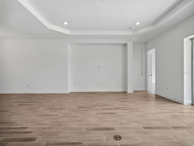 empty room featuring a raised ceiling and light hardwood / wood-style flooring