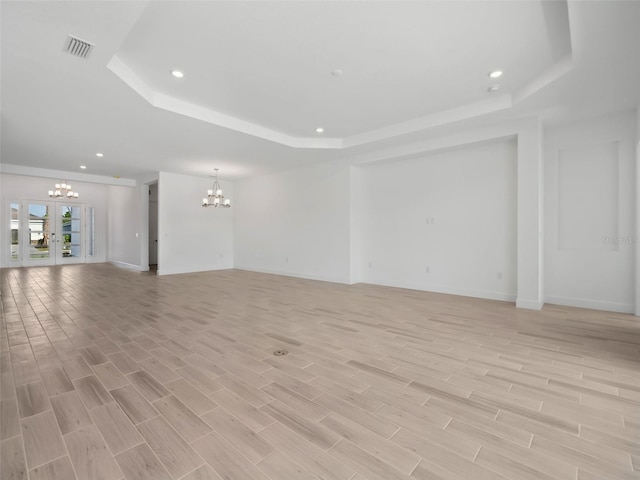 unfurnished living room with french doors, a chandelier, and a raised ceiling