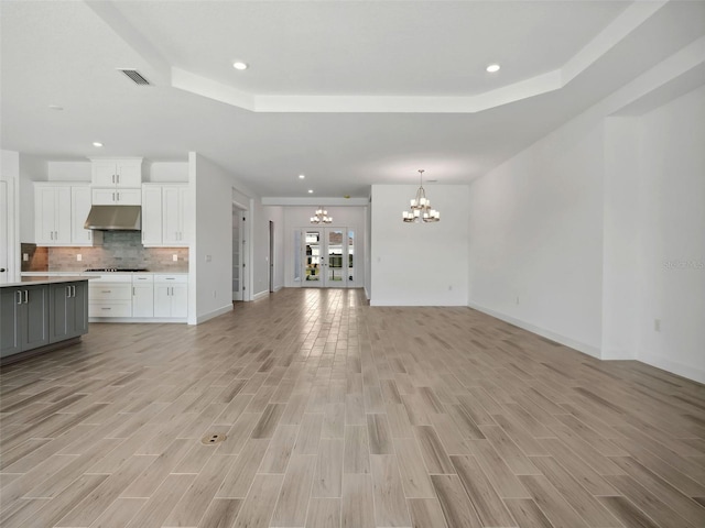 unfurnished living room featuring an inviting chandelier, a raised ceiling, and light wood-type flooring