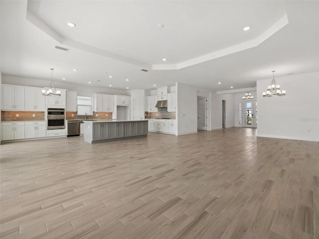 unfurnished living room featuring a raised ceiling, sink, an inviting chandelier, and light wood-type flooring