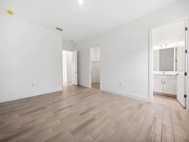 unfurnished bedroom with ensuite bathroom, a walk in closet, light hardwood / wood-style floors, and a closet