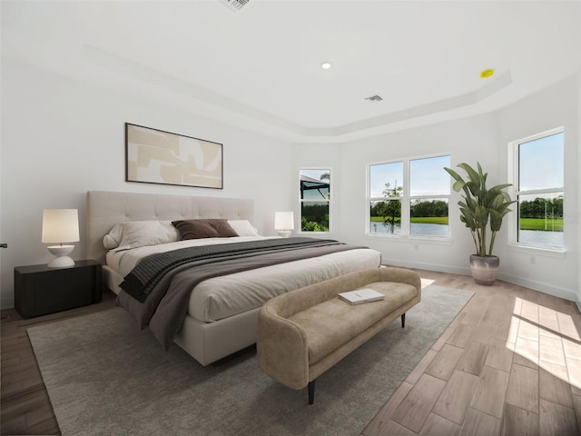 bedroom featuring a raised ceiling and light hardwood / wood-style floors