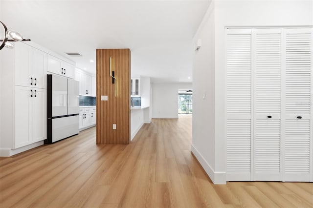 kitchen with freestanding refrigerator, white cabinets, backsplash, and light wood finished floors