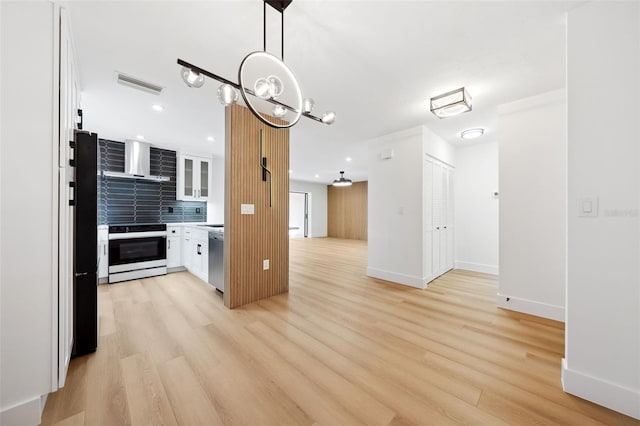 kitchen with hanging light fixtures, light wood-type flooring, appliances with stainless steel finishes, white cabinets, and wall chimney range hood